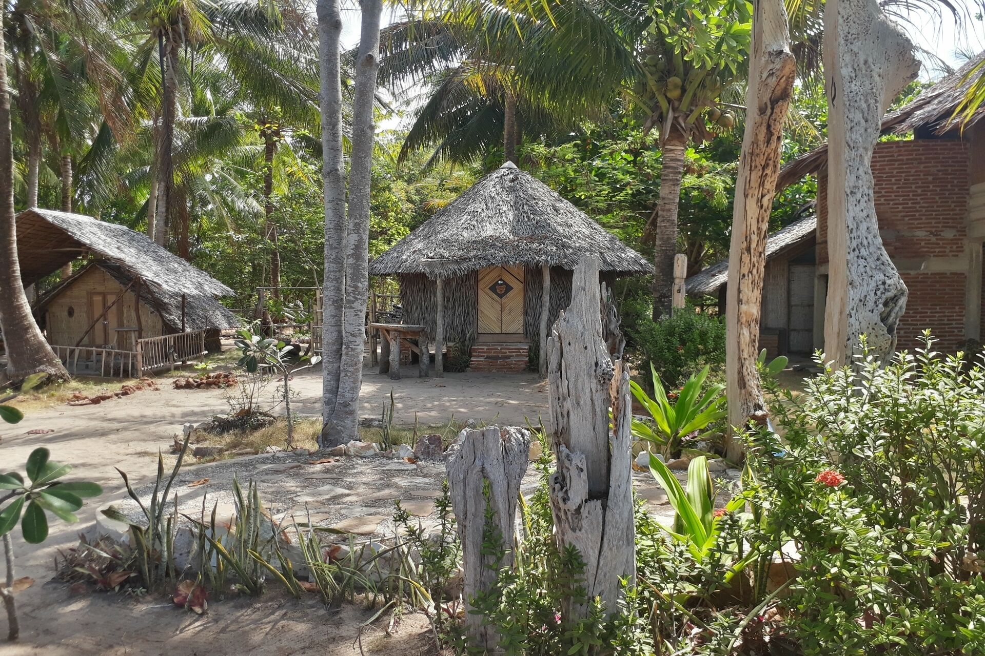 A rustic village scene with thatched-roof huts, a central hut with a wooden door, and surrounding greenery.