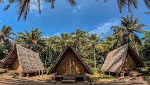 Three thatched-roof huts with a central door, surrounded by palm trees.