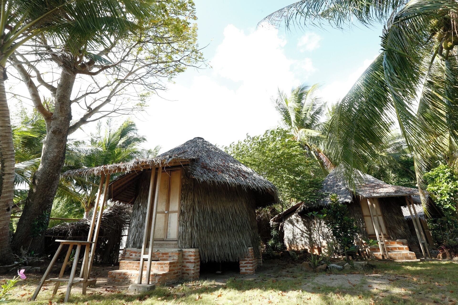 A traditional thatched-roof hut with a wooden door and a ladder leading to a brick platform.