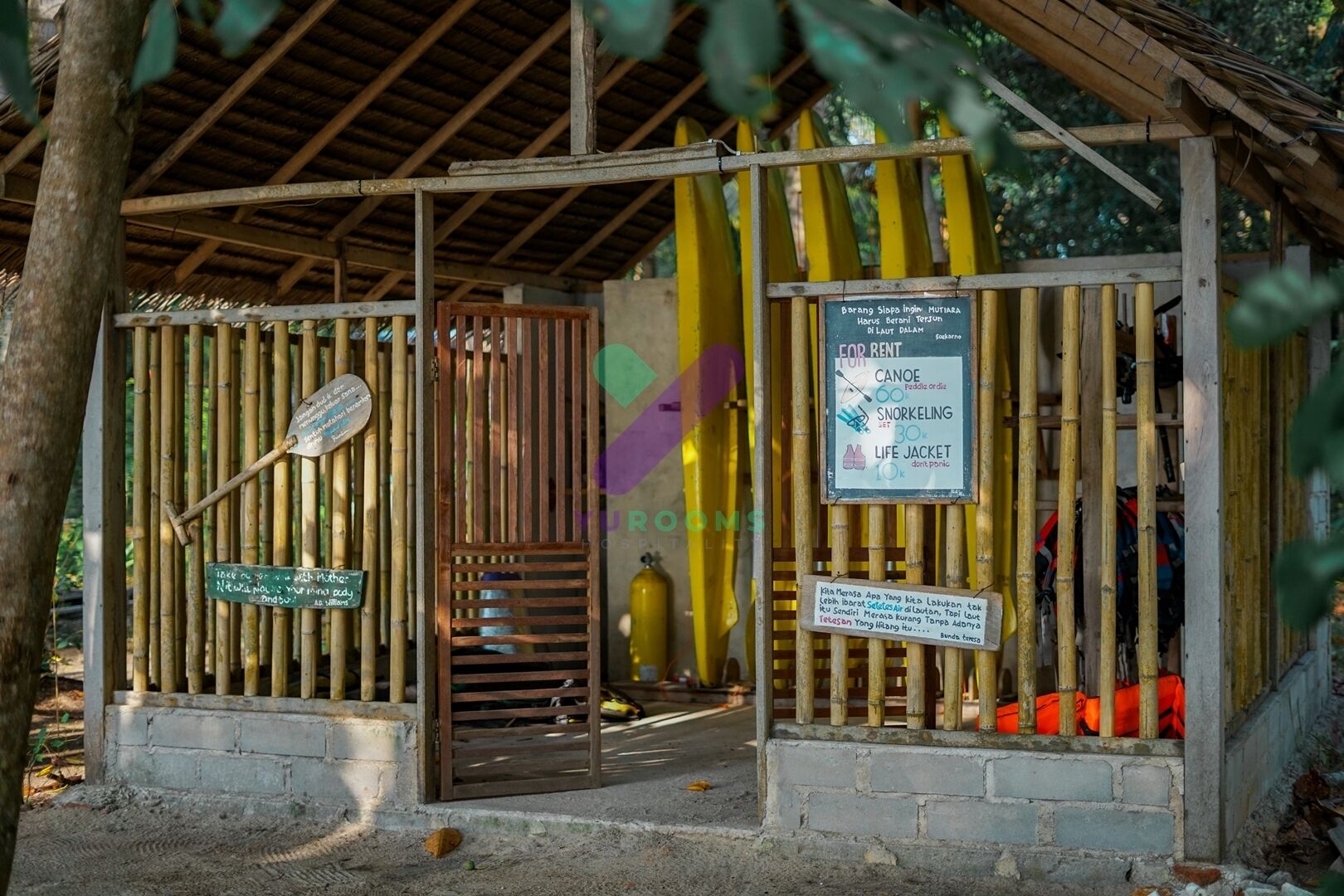 Une structure en bambou avec une pancarte indiquant les services de location de canoës, de matériel de plongée avec tuba et de gilets de sauvetage.