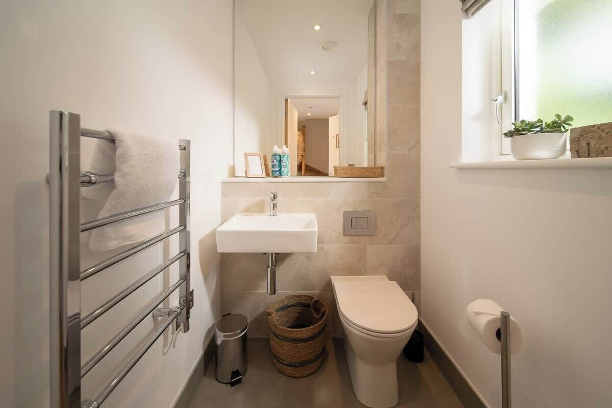 Un baño pequeño con toallero, lavabo, inodoro y una ventana con una planta.