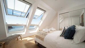 A bedroom with a large bed, skylights, a bench, and a view of the sea. - Panoramic Sea Views, Private Balcony & Sauna (Lynmouth)