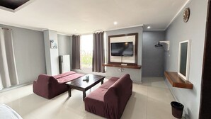 Una moderna camera d'albergo con divano, televisione a schermo piatto, un tavolino e una finestra con tende.