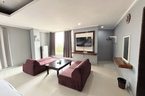 A modern hotel room with a sofa set, a flat-screen TV, a small table, and a window with curtains.