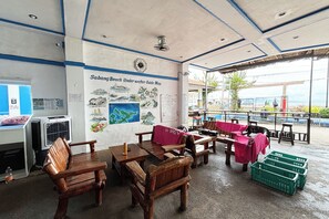 A beachside restaurant with wooden furniture, a guide map on the wall, and a view of the beach.