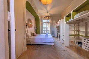 Quarto com cama, luminária de cabeceira e vista da cidade pela janela.