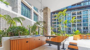 A modern outdoor area with a wooden bar, seating, and a view of a high-rise building. - Olympic Park Stylish 2BR | Walk to stadium | Pool & Gym (Lidcombe)