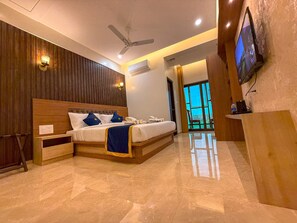 A modern hotel room with a large bed, a ceiling fan, a TV, and a view of the outdoors. - HOTEL COASTAL PALACE (Udupi)