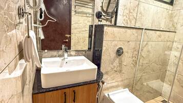 Un baño moderno con pared de mármol, tocador de madera, lavabo blanco, espejo y ducha con cerramiento de vidrio.