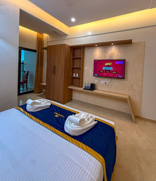 A hotel room with a bed, a television displaying a quiz, and a wooden wardrobe. - HOTEL COASTAL PALACE (Udupi)
