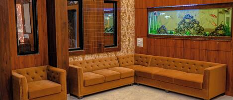 Eine Sitzecke mit einem braunen Ledersofa und einem kleineren Sessel, einem großen Aquarium mit Fischen und Holzvertäfelung.