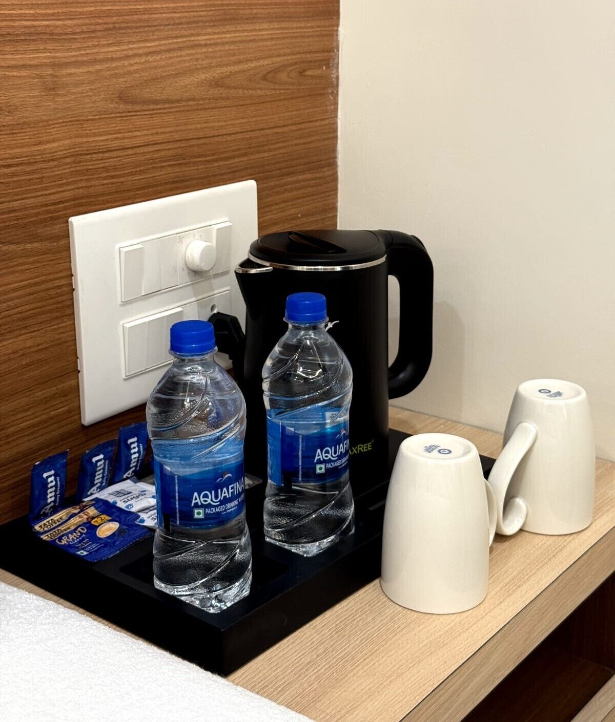 Une chambre d’hôtel avec un plateau noir sur lequel se trouvent deux bouteilles d’eau Aquafina, une machine à café noire et deux tasses blanches.