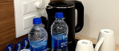 Une chambre d’hôtel avec un plateau noir sur lequel se trouvent deux bouteilles d’eau Aquafina, une machine à café noire et deux tasses blanches.