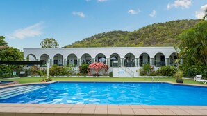 Una piscina con un edificio blanco al fondo, que presenta ventanas arqueadas.