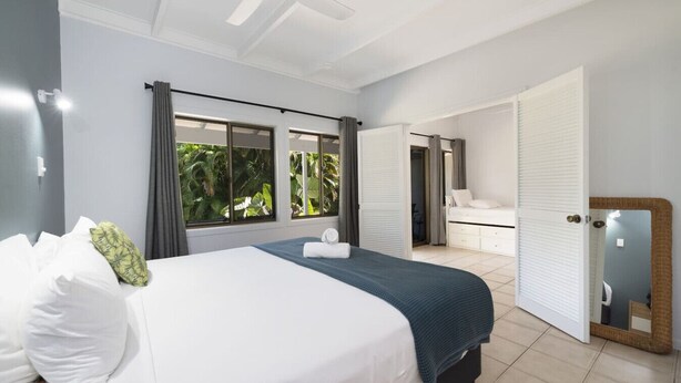 Een slaapkamer met een bed, een plafondventilator, een raam met gordijnen, een deur naar een andere kamer en een spiegel.