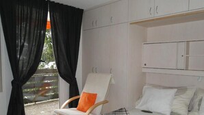 A bedroom with a bed, a chair with an orange cushion, and a window with black curtains. - Apartment 'Studio in Sankt Blasien' with Balcony and Wi-Fi (St Blasien)