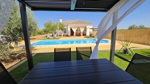 Une terrasse couverte avec une piscine, des sièges d’extérieur et une vue sur une maison en arrière-plan.