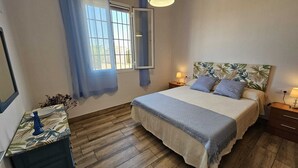 Une chambre à coucher comprenant un lit, des tables de chevet, une commode, une fenêtre avec des rideaux et un miroir.