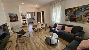 Un salon moderne avec un canapé noir, une table basse ronde et un coin repas comprenant une table et des chaises en bois.