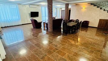 A spacious living area with a polished tile floor, a dining table with chairs, a sofa, and a staircase with a railing.