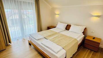 Habitación de hotel con una cama grande, suelo de madera, una lámpara de techo y una ventana con cortinas.