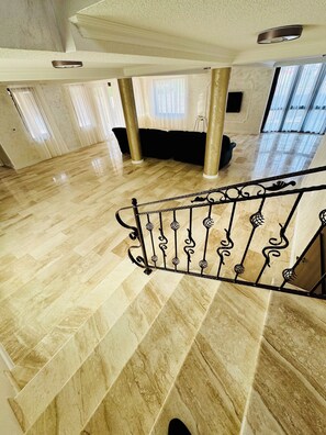 A spacious room with a marble floor, a black sofa, and a staircase with ornate railings. - Roua Residence (Vladimirescu)