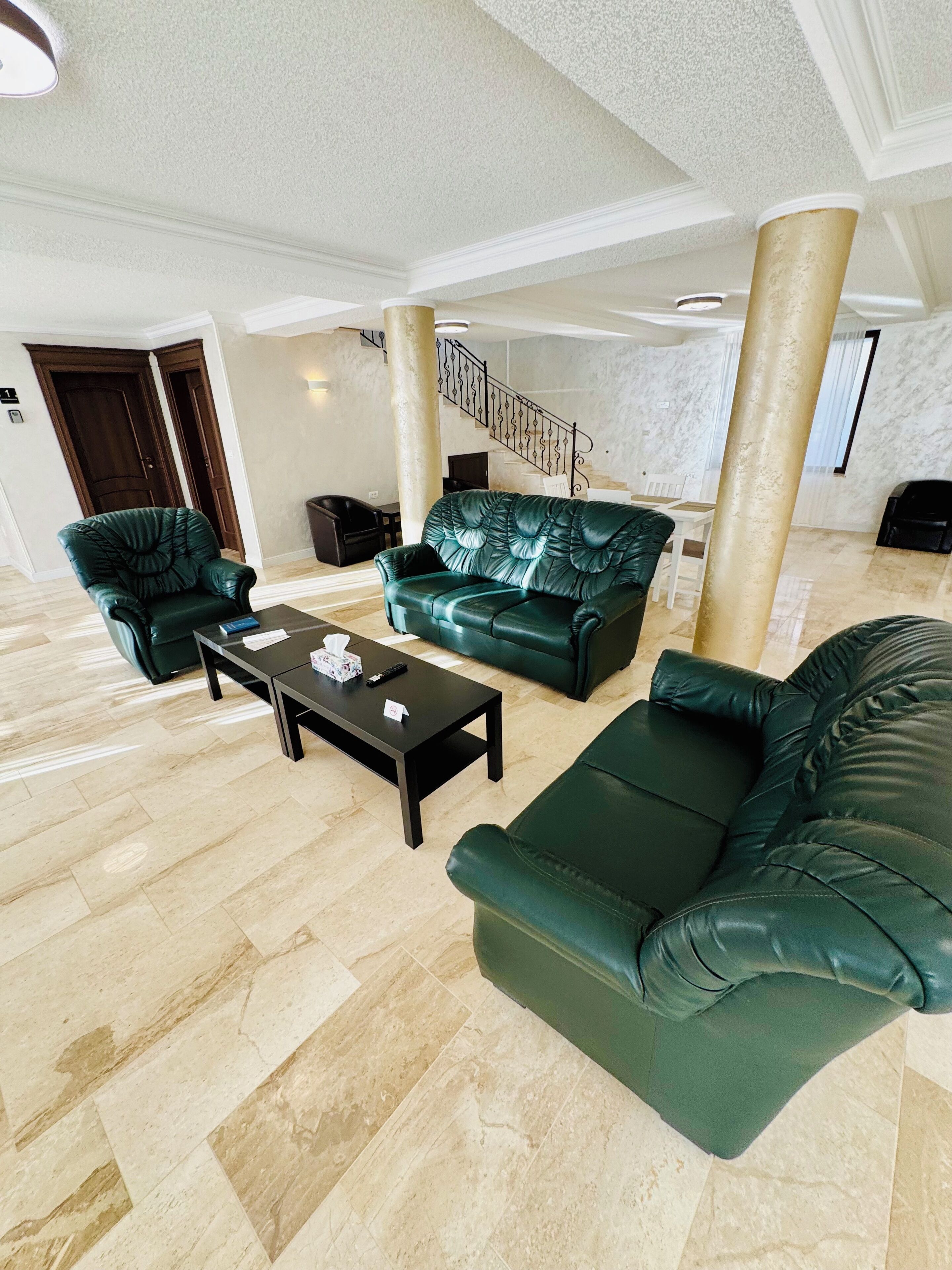 A spacious living area with a high ceiling, a marble staircase, and a view of the sky.