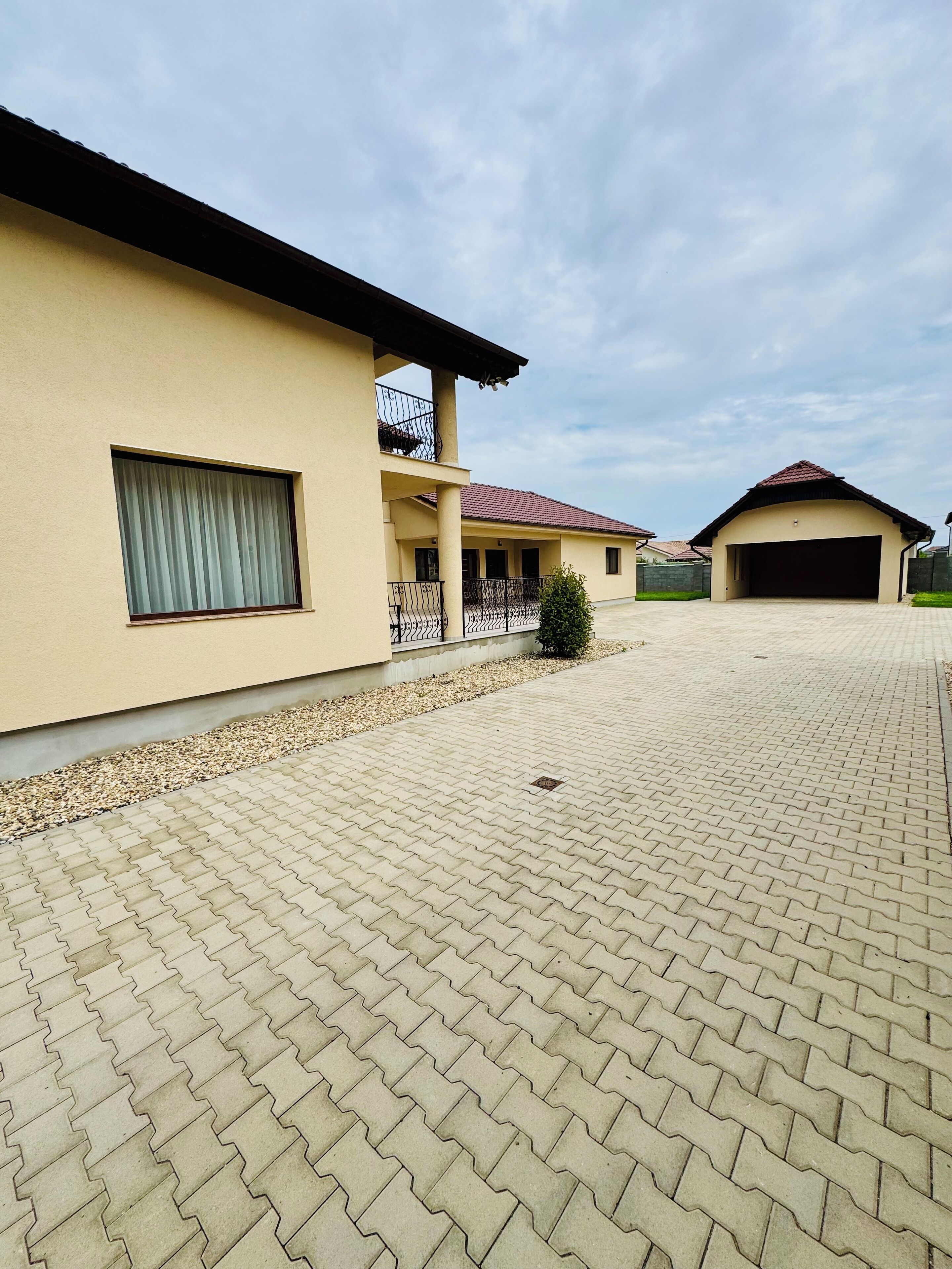 Un edificio residencial con entrada pavimentada, garaje cubierto y balcón con barandilla.