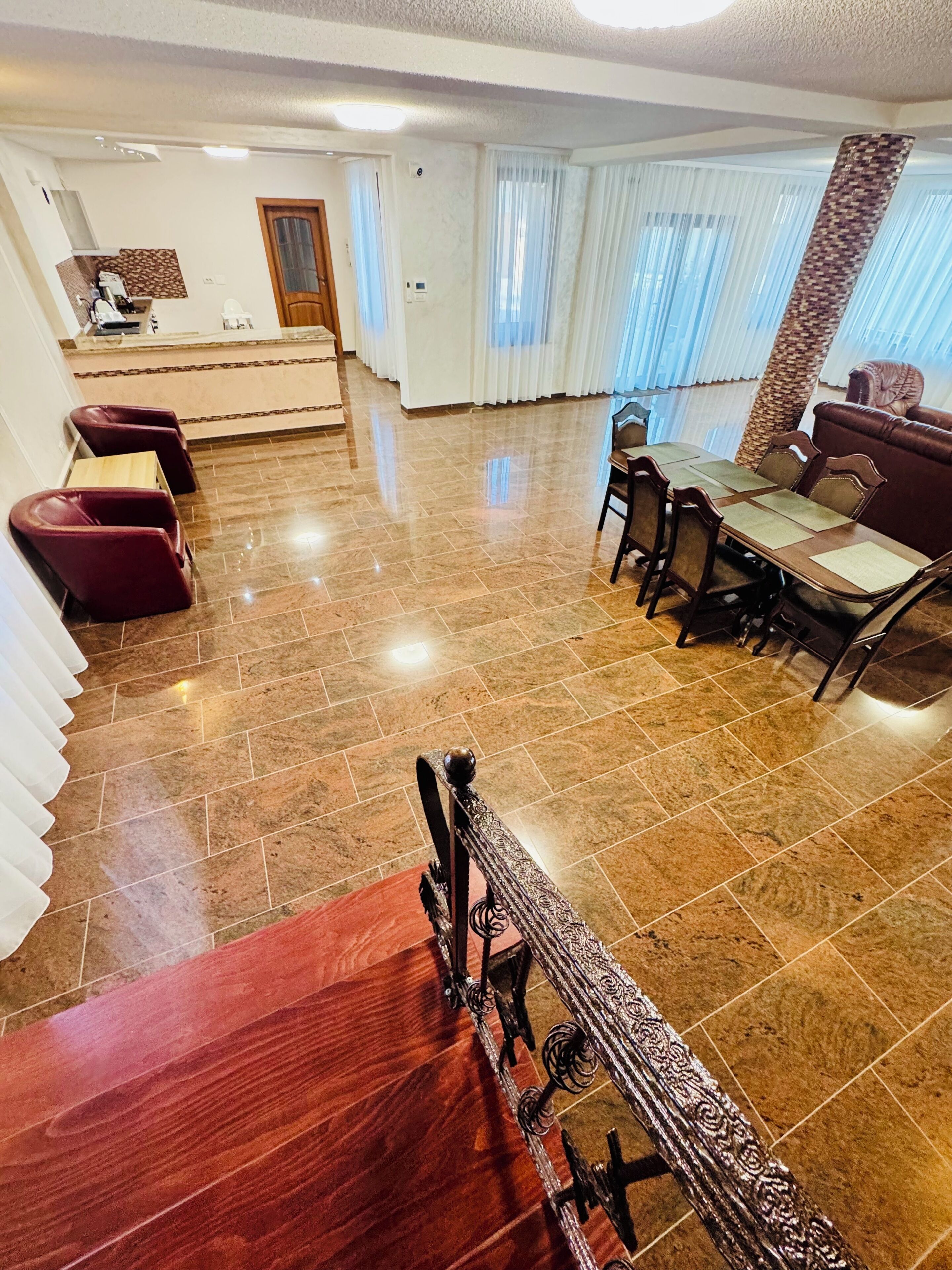 Un comedor amplio con una mesa y sillas de madera, una zona de estar separada con sillas rojas y una cocina al fondo.