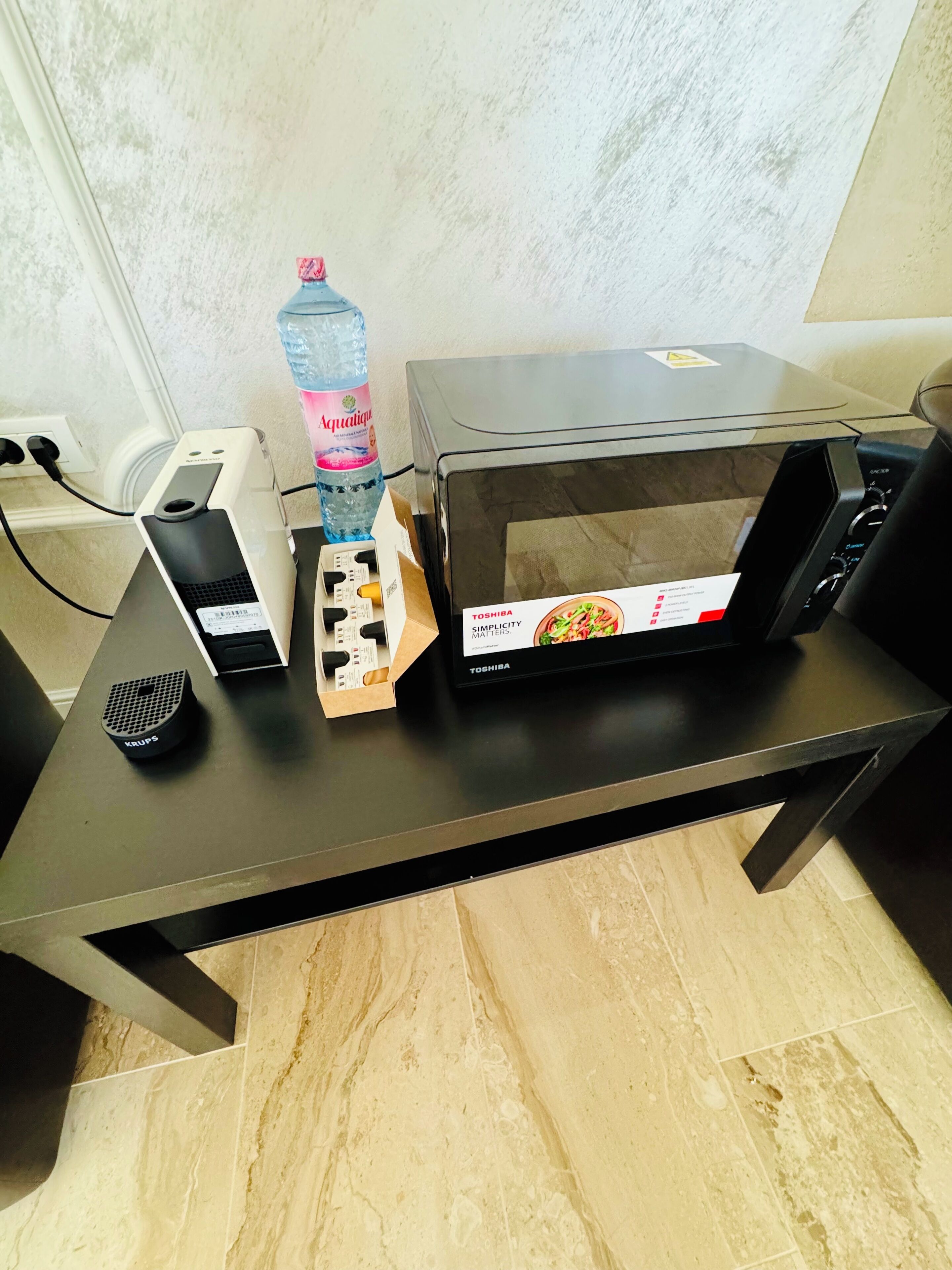 Een keukenhoek met een magnetron, een waterfles en een speaker op een tafel.