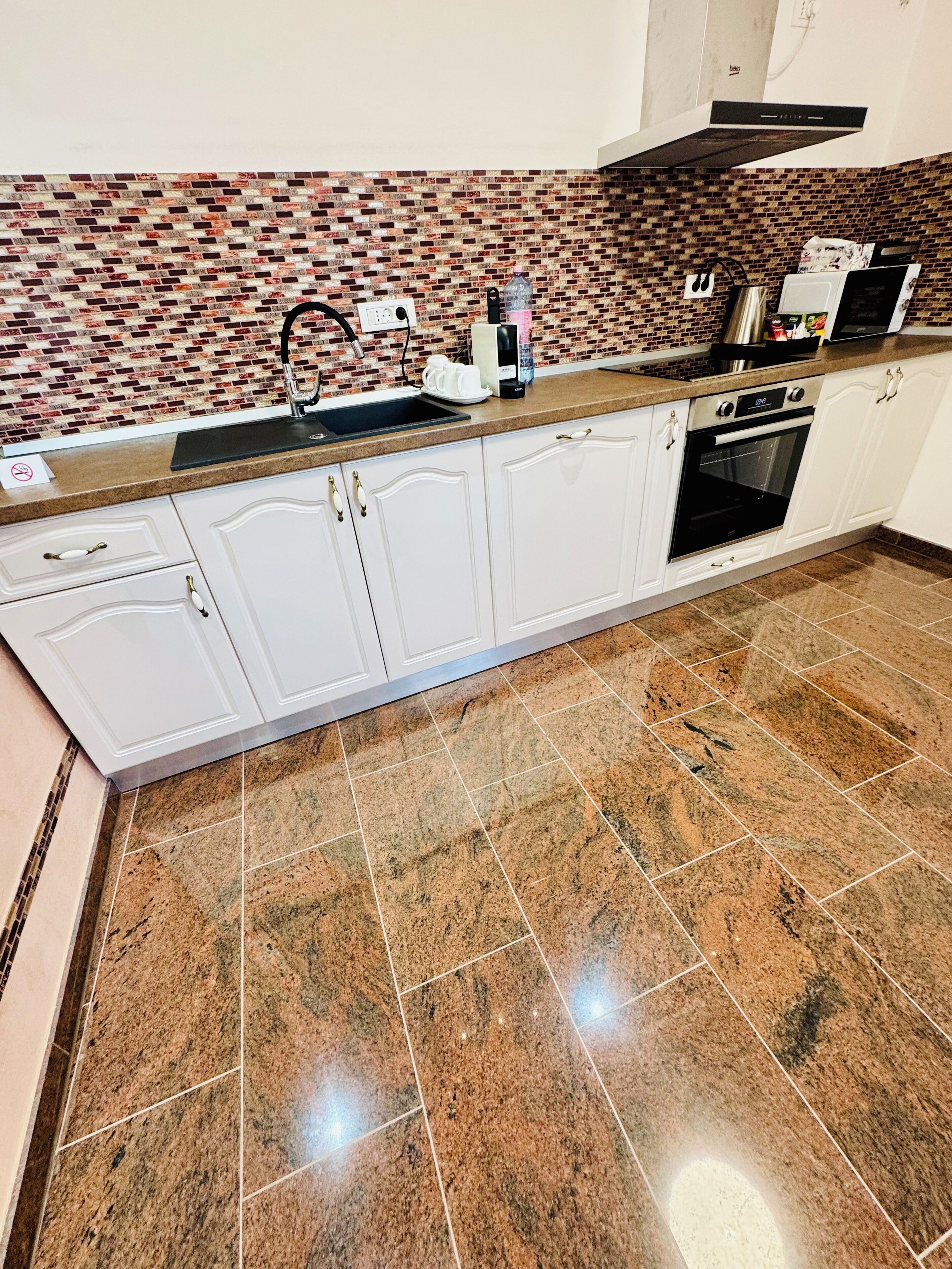A kitchen with white cabinets, a granite countertop, a brick backsplash, and a built-in oven.
