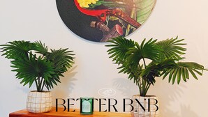 Una estantería de madera con dos plantas en macetas y una obra de arte circular colgada en la pared, con un pájaro y follaje.