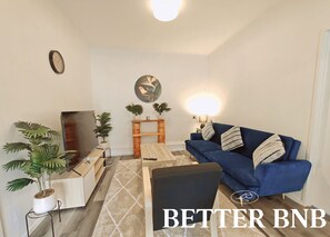 A modern living room with a blue sofa, a wooden coffee table, a TV, and potted plants. - Affordable Value Semi-Detached Home · 2BR · 3 Beds (Lower Hutt)