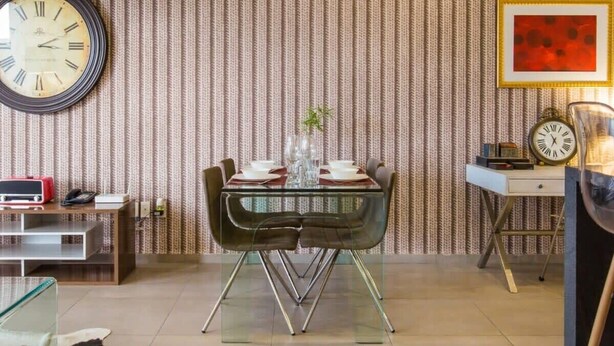 Un coin repas avec une table en verre, des chaises noires et une horloge au mur.