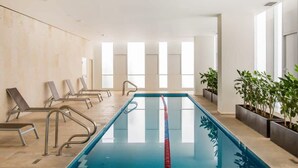 Une piscine avec de grandes fenêtres baignées de lumière, des chaises longues et des plantes en pot.