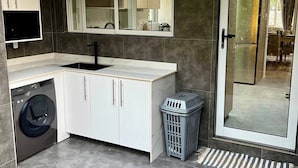 Une cuisine moderne équipée d’un lave-linge encastré, d’un évier et d’un grand miroir au-dessus du plan de travail.