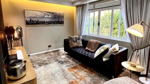 Un salon moderne avec un canapé foncé, une table basse, une lampe et un tableau représentant un paysage urbain accroché au mur.