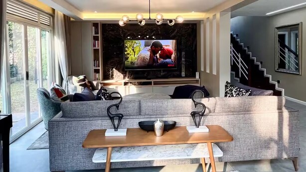 Un salon moderne avec un grand téléviseur à écran plat, un canapé gris, une table basse en bois et un escalier en arrière-plan.