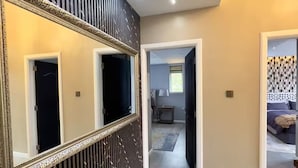 Un couloir avec un grand miroir, un panneau décoratif noir et une porte donnant sur une chambre à coucher.