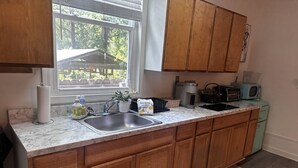 Una cocina con armarios de madera, encimera de mármol, pileta, microondas y una ventana con persianas.