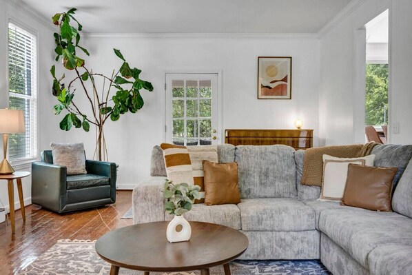 Een woonkamer met een hoekbank, een klein rond tafeltje en een grote plant.