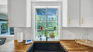 Eine Küche mit großem Fenster, Holz Arbeitsplatten, weißen Schränken und einer schwarzen Spüle.
