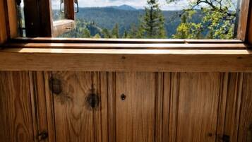 A window with a view of a forest and mountains, a wooden interior, and a white mug with 'HAUKEBU' text.