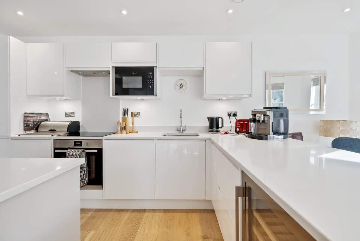 A modern kitchen with white cabinetry, a built-in microwave, a coffee machine, and a sink.