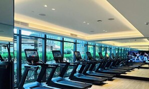 Ein Fitnessstudio mit Laufbändern vor Glaswänden, das Ausblick auf Grünflächen bietet.