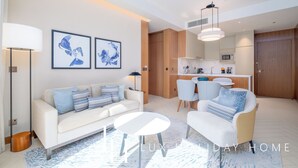 A modern living room with a sofa, coffee table, and chairs, a kitchen area with cabinets and a microwave, and artwork on the walls. - LUX  The Address Opera Downtown Suite (Dubai)