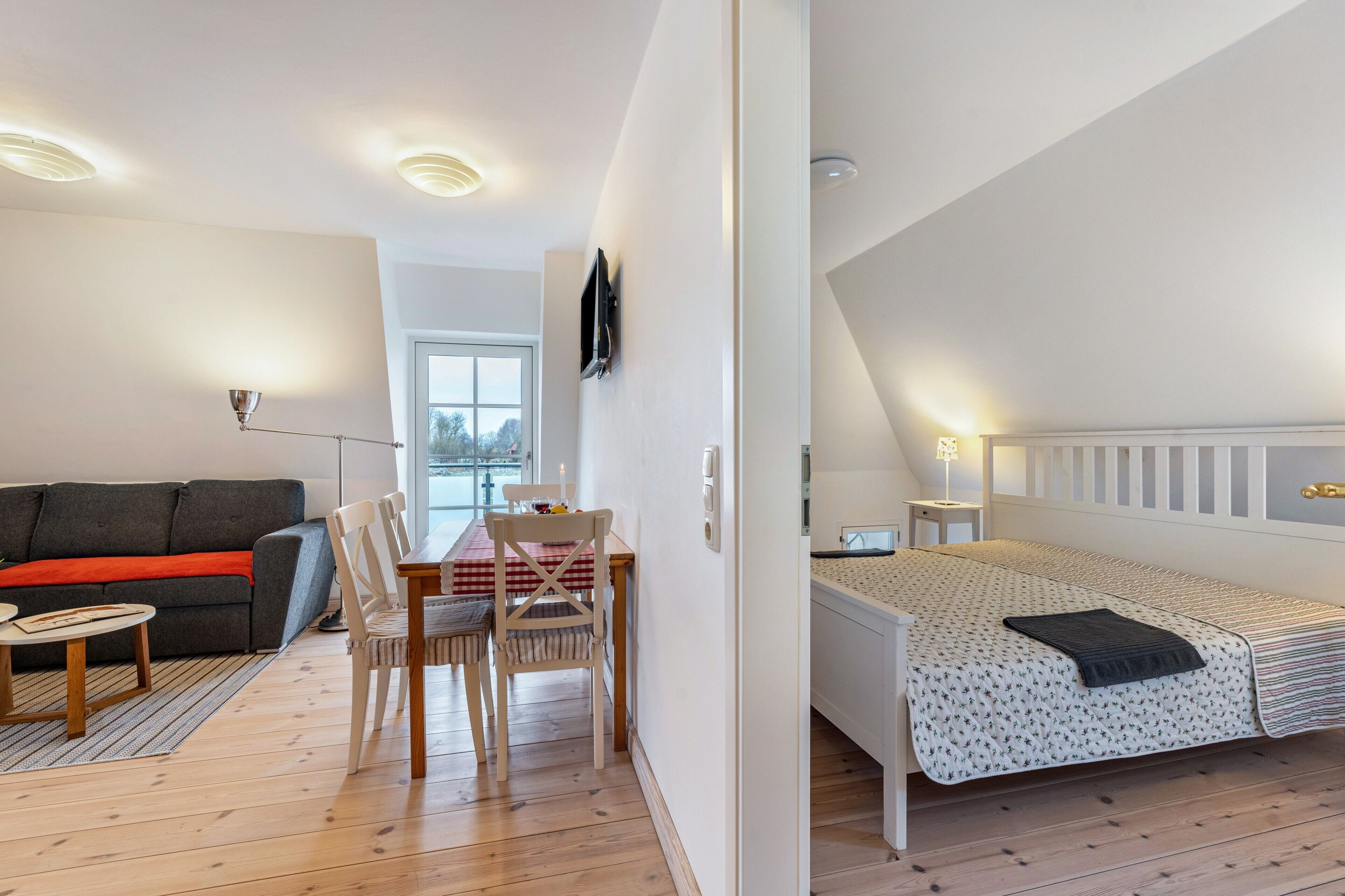Ein modernes Zimmer mit einer Couch, einem Esstisch, Stühlen, einem Bett und einem an der Wand befestigten Fernseher.