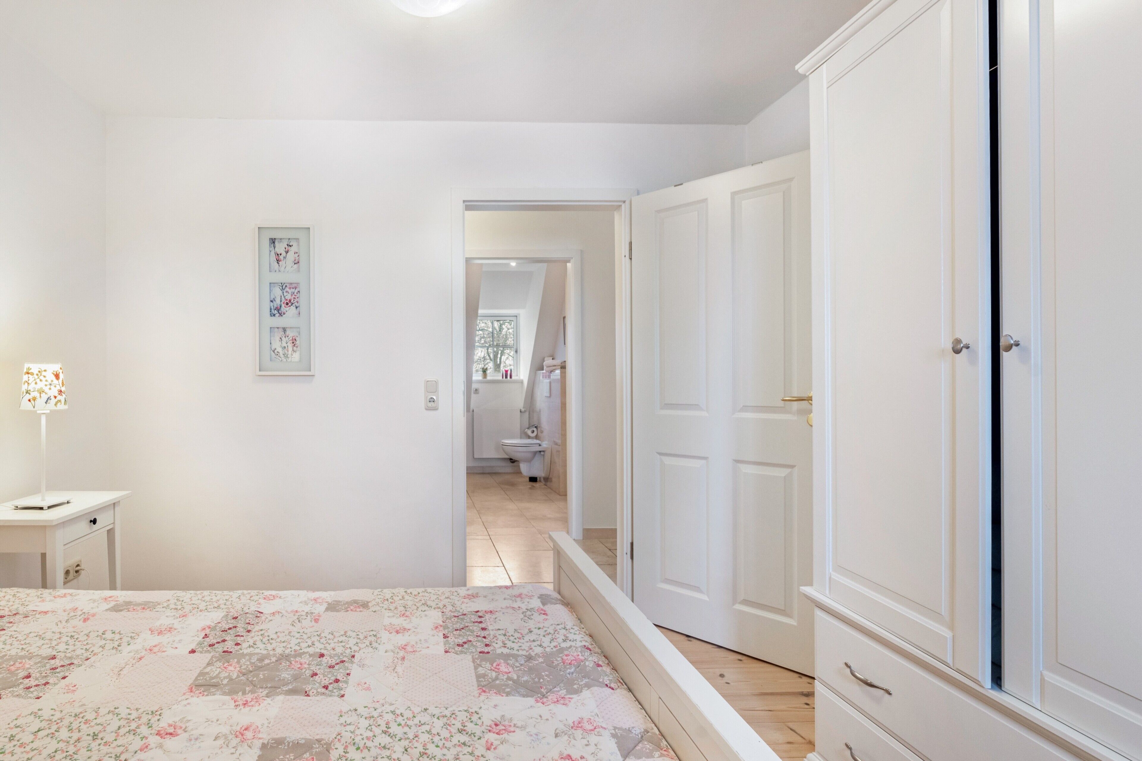 Une chambre à coucher comprenant un lit, une table de chevet, une armoire et une porte donnant sur une salle de bain.
