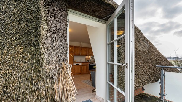 Een gebouw met rieten dak en een modern interieur, inclusief een keuken en een glazen entree.