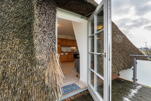 Um edifício com telhado de palha e interior moderno, incluindo cozinha e entrada por porta de vidro.